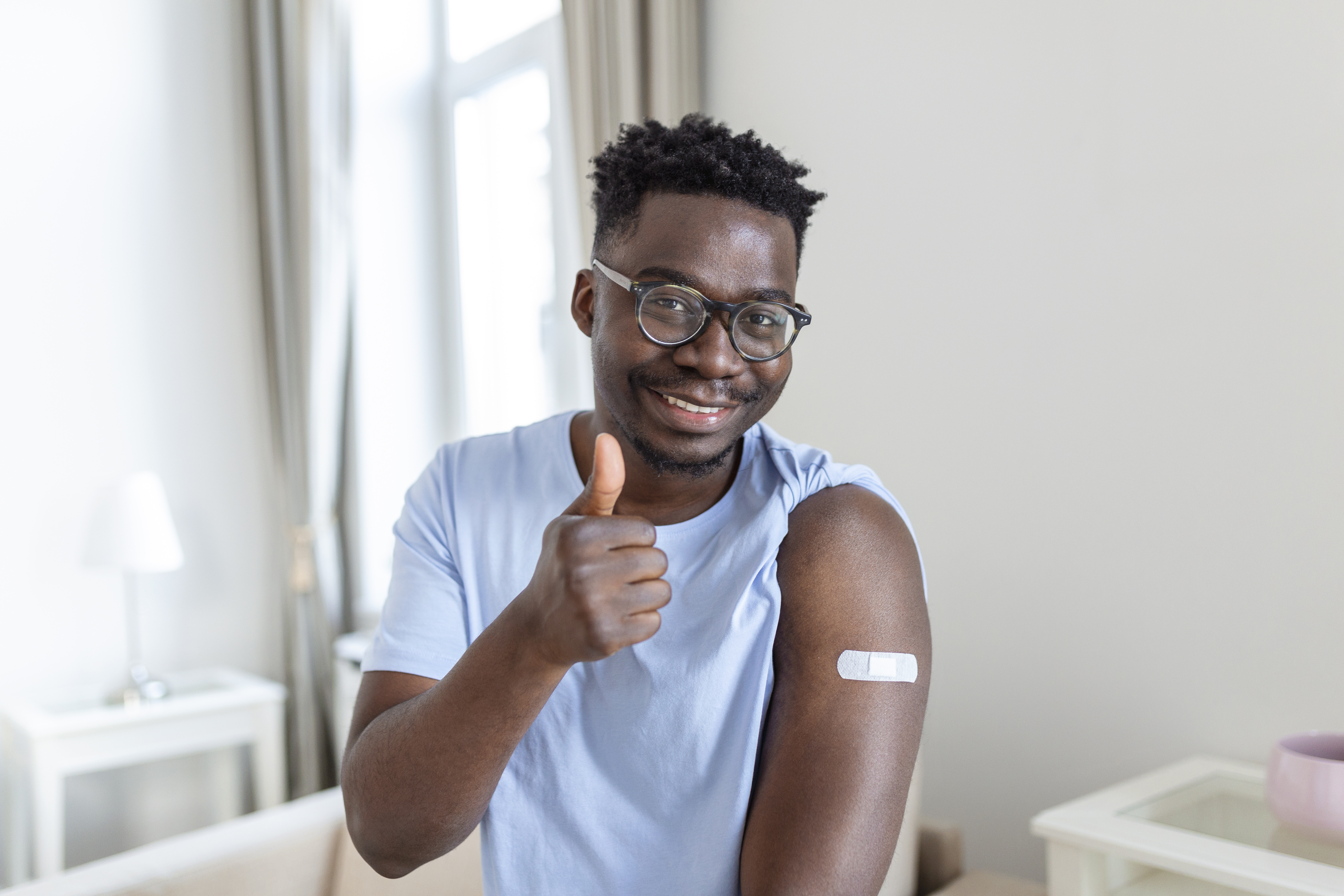 Portrait of a man smiling after getting a vaccine. African man holding down his shirt sleeve and showing his arm with bandage after receiving vaccination.
